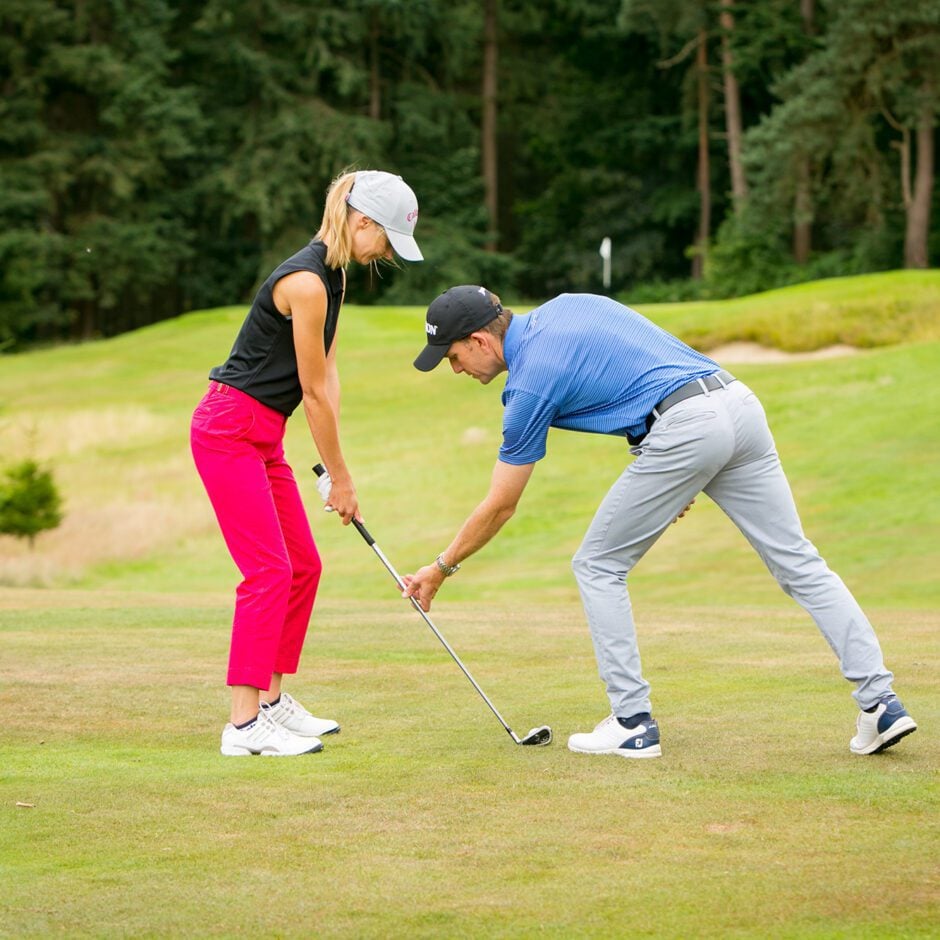 Golf Academy - Man in blue t-shirt showing woman in black sleeveless t-shirt how to position a golf club