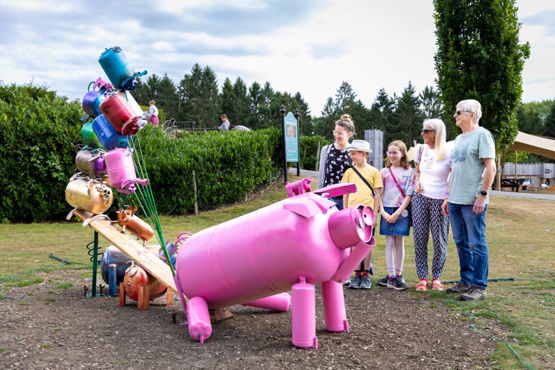 People exploring the sculpture trail at Leed's Castle, looking at a pink metal pig.